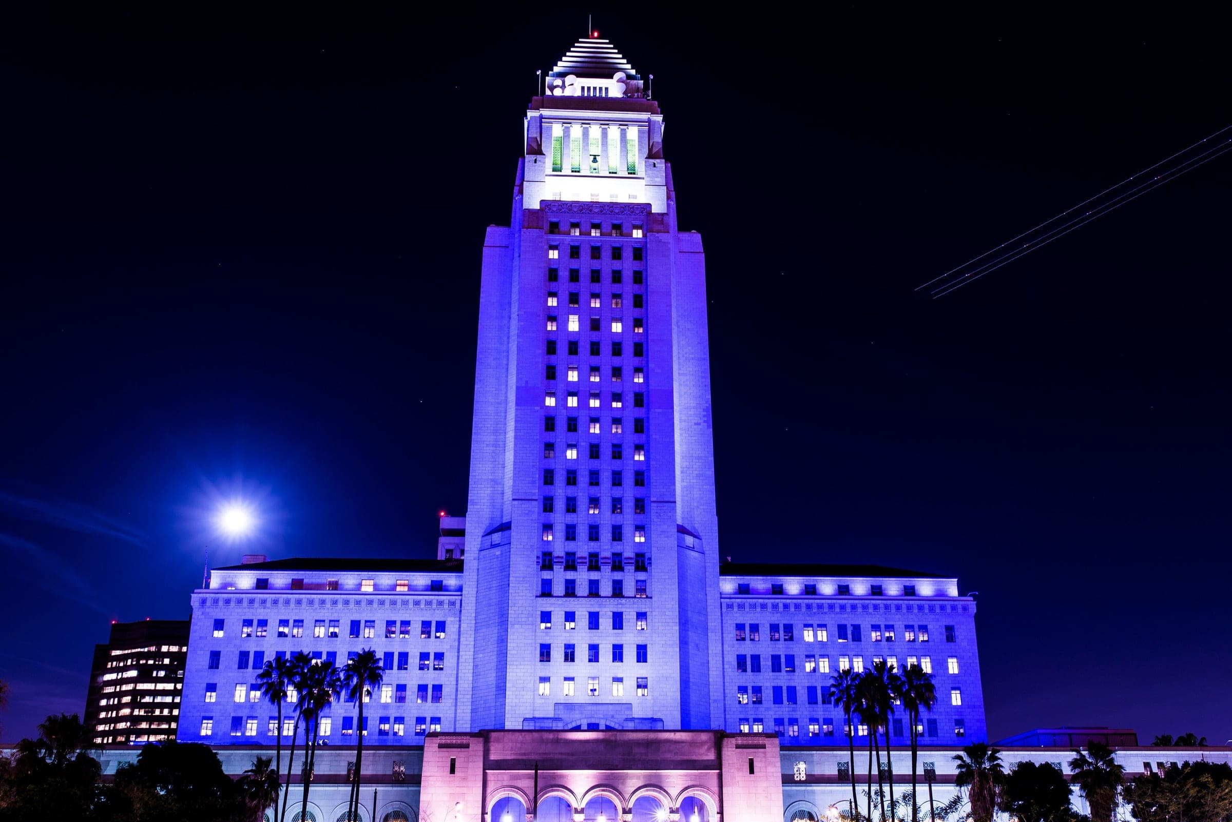 Die City Hall von Los Angeles, nachts lila angestrahlt, daneben der Mond